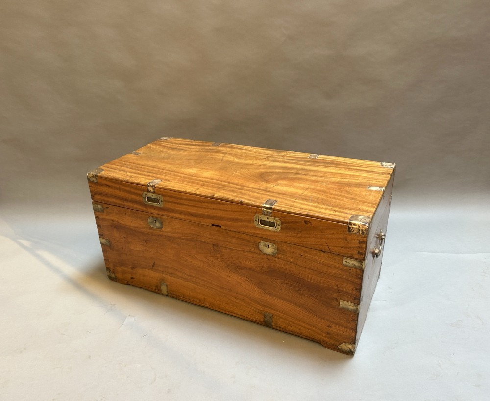 A rectangular 19th-century camphor wood campaign trunk featuring corner brass bindings, flush-fitting handles, and keyhole escutcheons.