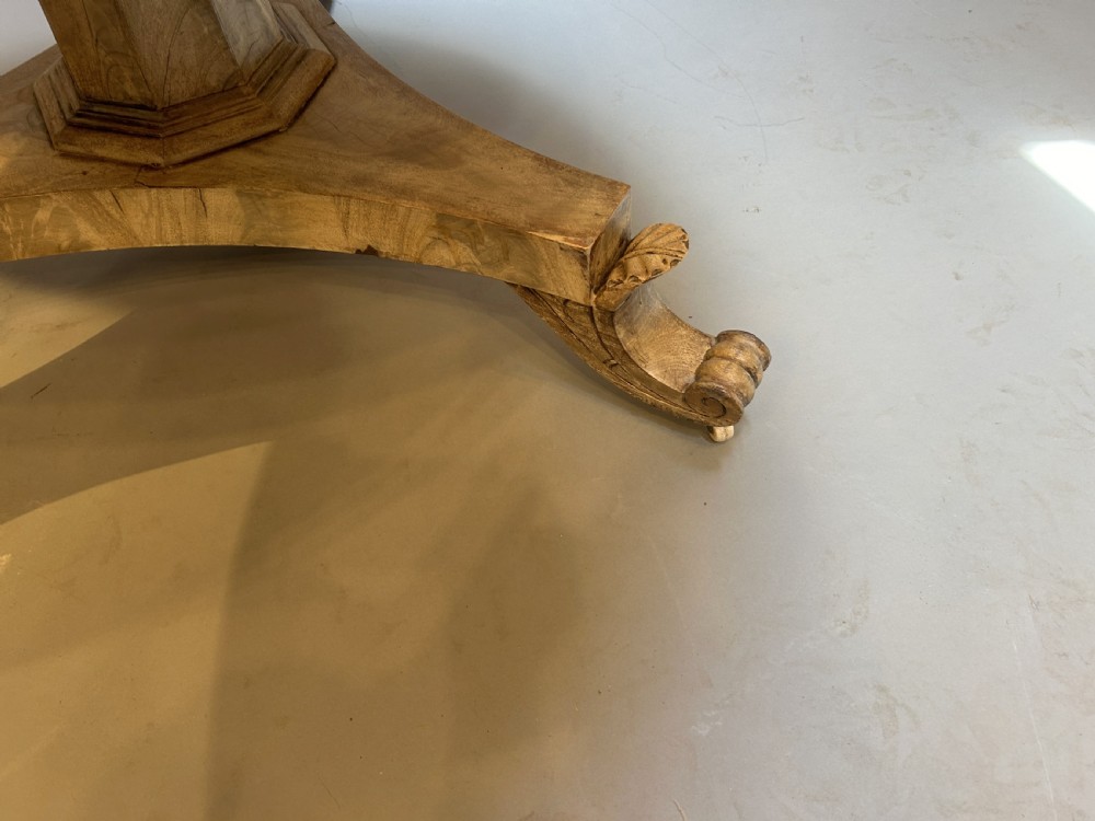 A 19th-century circular dining table featuring a radially veneered top, a faceted central pedestal column, and a carved triform base with scroll feet. View V