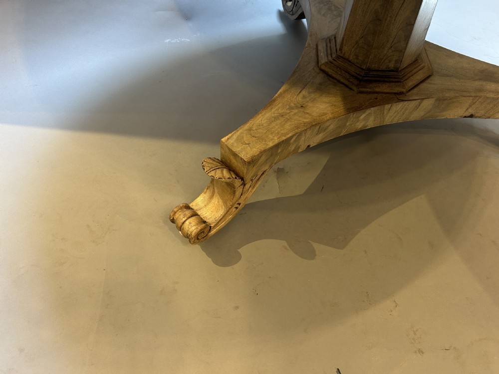 A 19th-century circular dining table featuring a radially veneered top, a faceted central pedestal column, and a carved triform base with scroll feet. View VII