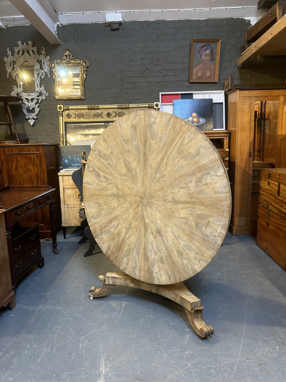 A 19th-century circular dining table featuring a radially veneered top, a faceted central pedestal column, and a carved triform base with scroll feet. View VIII