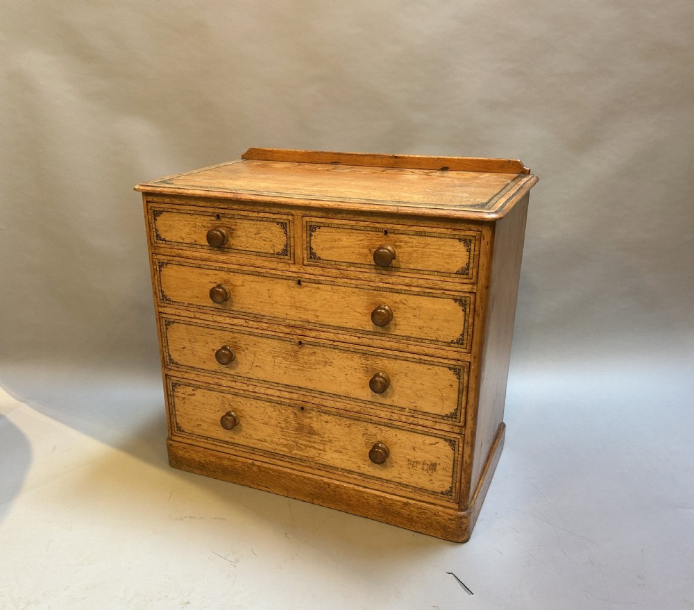 A Victorian warm pine chest of drawers featuring a two over three drawer arrangement decorated with black stencilled line borders and turned wooden handles.