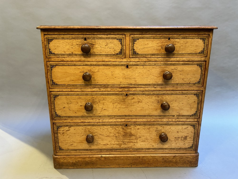 A Victorian pine chest of drawers with black stencilled borders, featuring two short drawers over three long drawers with turned wooden knobs.