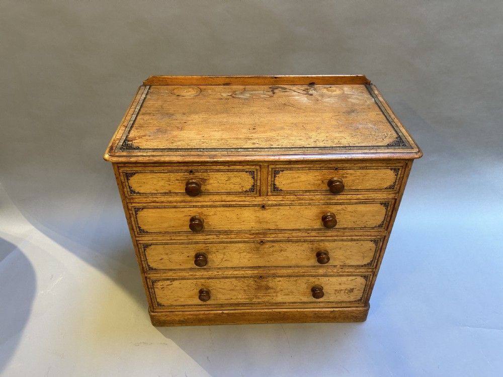 A Victorian pine chest of drawers with black stencilled borders, featuring two short drawers over three long drawers with turned wooden knobs. View II