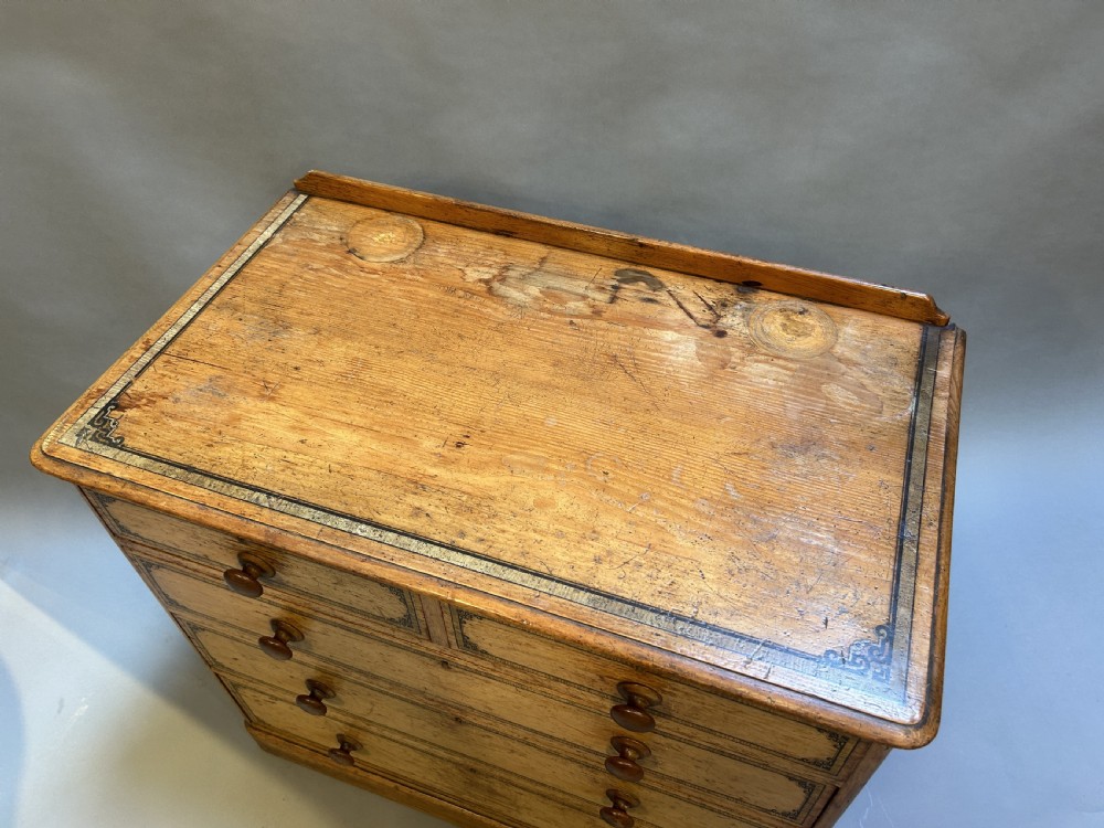 A Victorian pine chest of drawers with black stencilled borders, featuring two short drawers over three long drawers with turned wooden knobs. View III