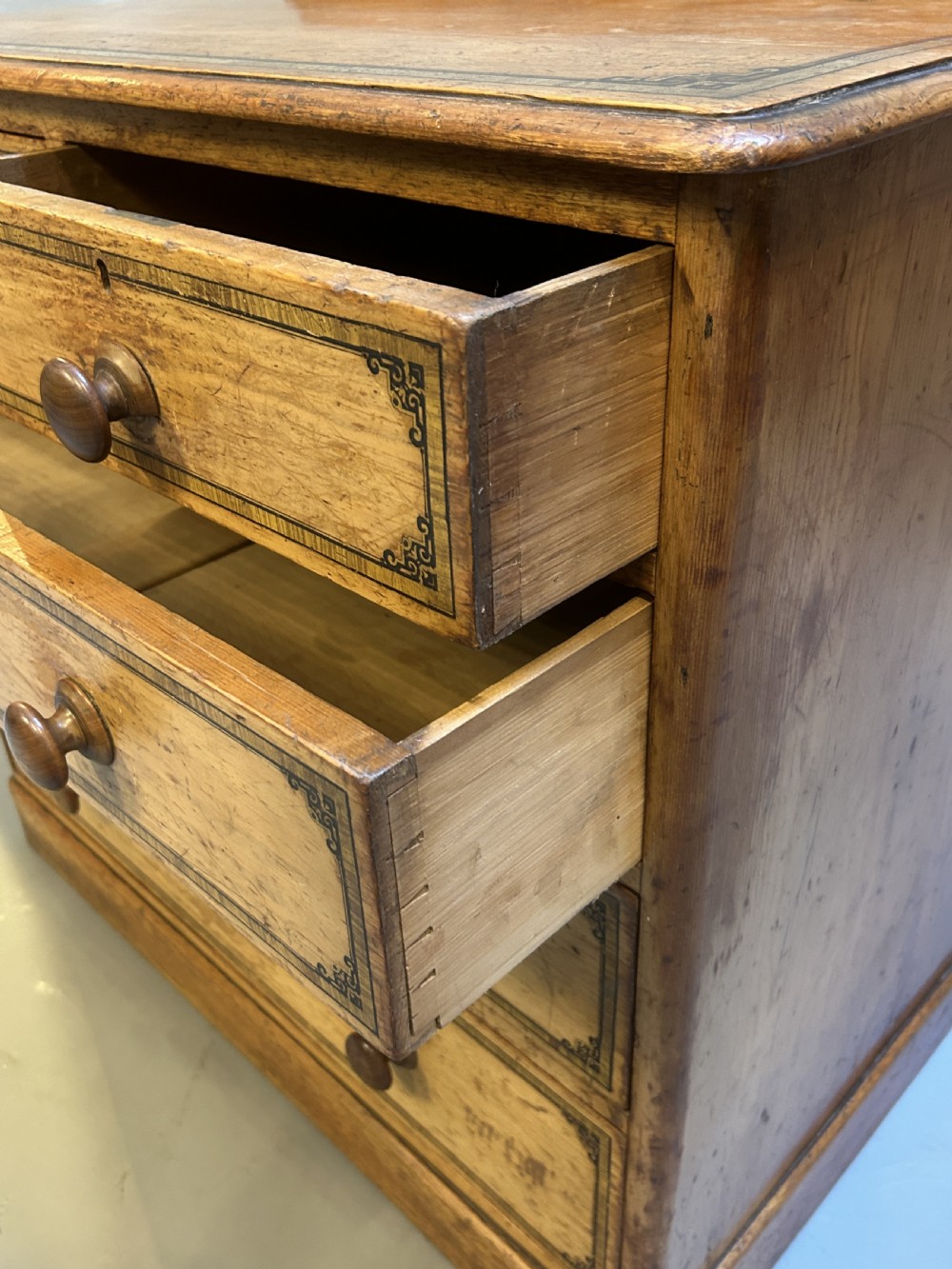 A Victorian pine chest of drawers with black stencilled borders, featuring two short drawers over three long drawers with turned wooden knobs. View IV
