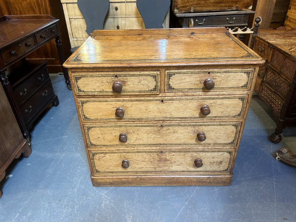 A Victorian pine chest of drawers with black stencilled borders, featuring two short drawers over three long drawers with turned wooden knobs. View VI