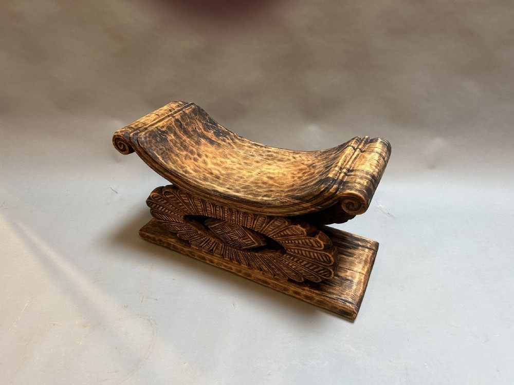 A hand-carved wooden Ashanti stool featuring a crescent-shaped seat with scroll ends, an openwork carved central support, and a flat rectangular base.