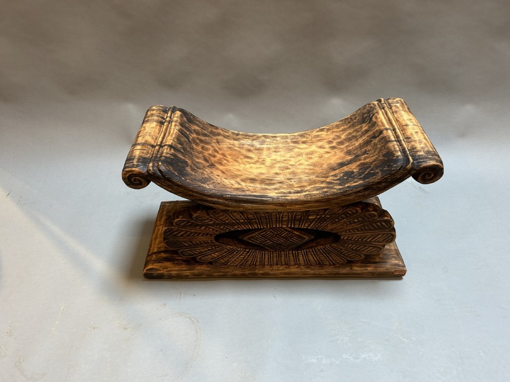 A hand-carved wooden Ashanti stool featuring a crescent-shaped seat with scroll ends, an openwork carved central support, and a flat rectangular base. View II