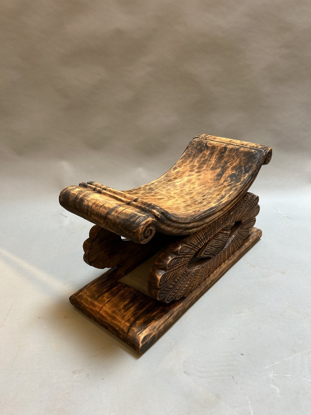 A hand-carved wooden Ashanti stool featuring a crescent-shaped seat with scroll ends, an openwork carved central support, and a flat rectangular base. View III