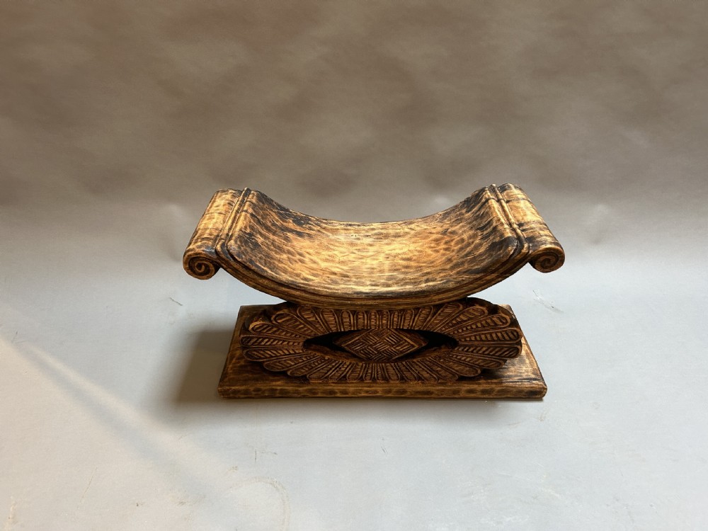 A hand-carved wooden Ashanti stool featuring a crescent-shaped seat with scroll ends, an openwork carved central support, and a flat rectangular base. View IV