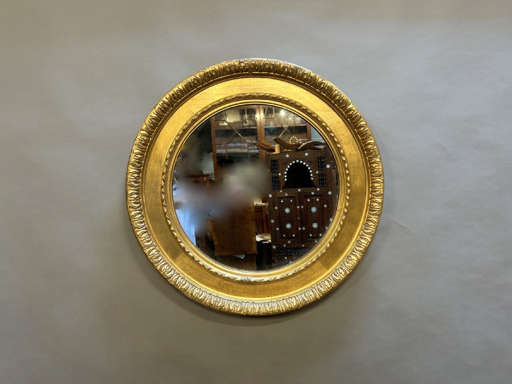 A circular Victorian wall mirror featuring a carved gold gilt frame with moulded gadrooned detail.