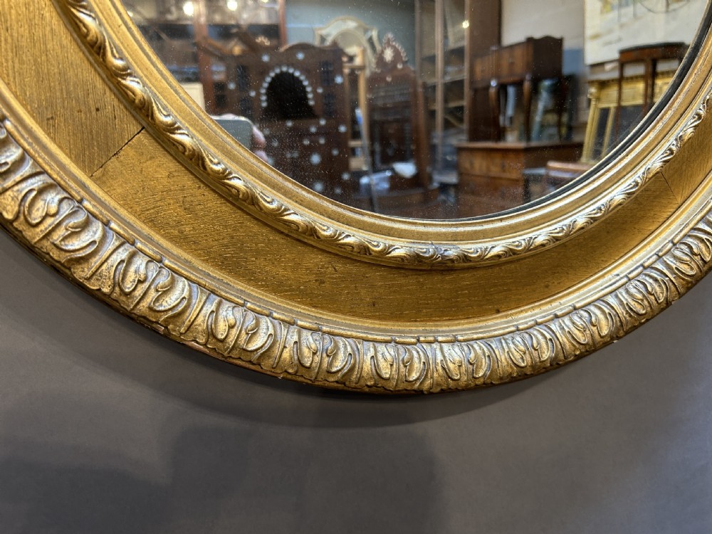 A circular Victorian wall mirror featuring a carved gold gilt frame with moulded gadrooned detail. View V