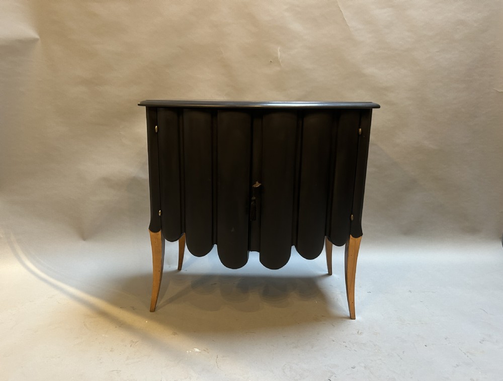 A French Art Deco black ebonised side cabinet with fluted doors, brass key hardware, and tapered light-coloured legs.
