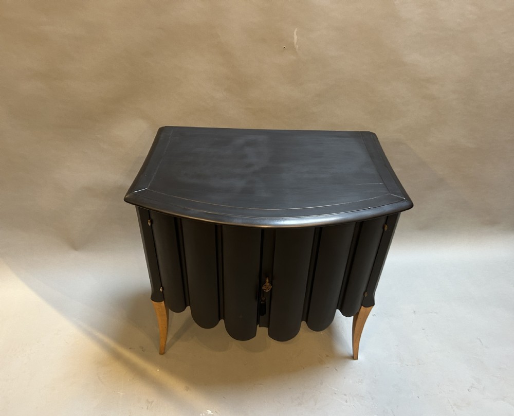 A French Art Deco black ebonised side cabinet with fluted doors, brass key hardware, and tapered light-coloured legs. View II