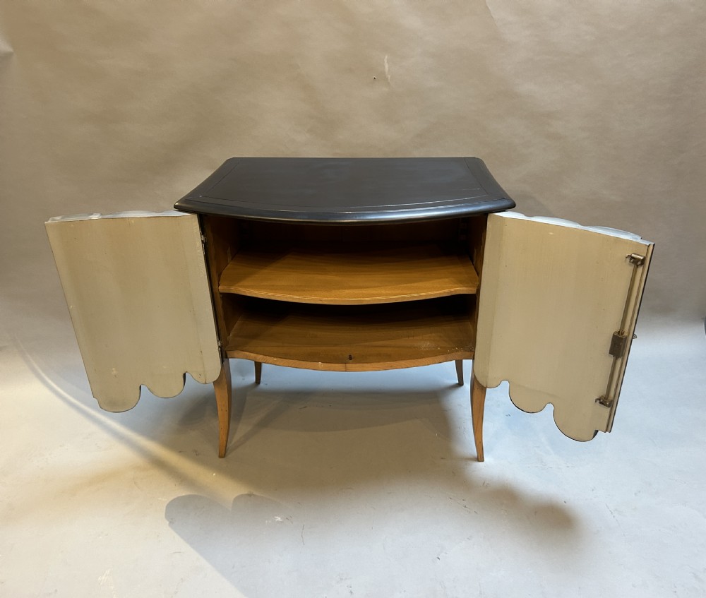 A French Art Deco black ebonised side cabinet with fluted doors, brass key hardware, and tapered light-coloured legs. View V