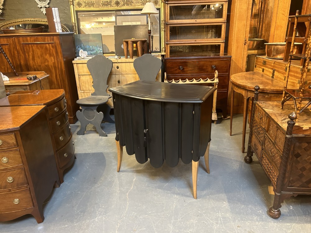 A French Art Deco black ebonised side cabinet with fluted doors, brass key hardware, and tapered light-coloured legs. View VI