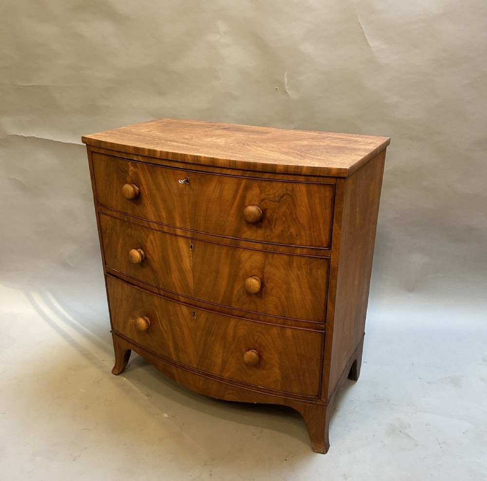 A George III bow front chest of drawers in warm brown timber, featuring three graduated drawers with turned wooden handles and splayed feet.