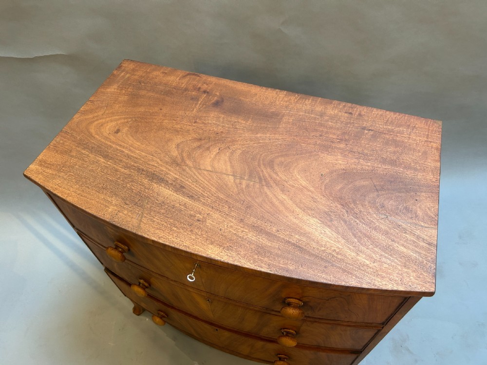 A George III bow front chest of drawers in warm brown timber, featuring three graduated drawers with turned wooden handles and splayed feet. View II