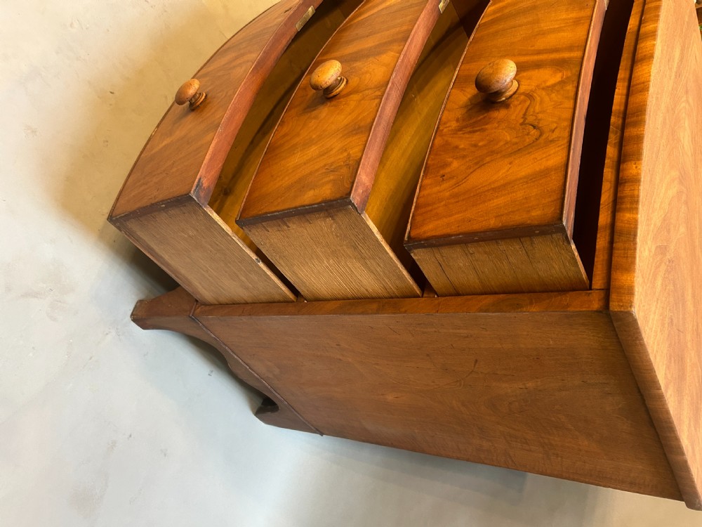 A George III bow front chest of drawers in warm brown timber, featuring three graduated drawers with turned wooden handles and splayed feet. View VIII