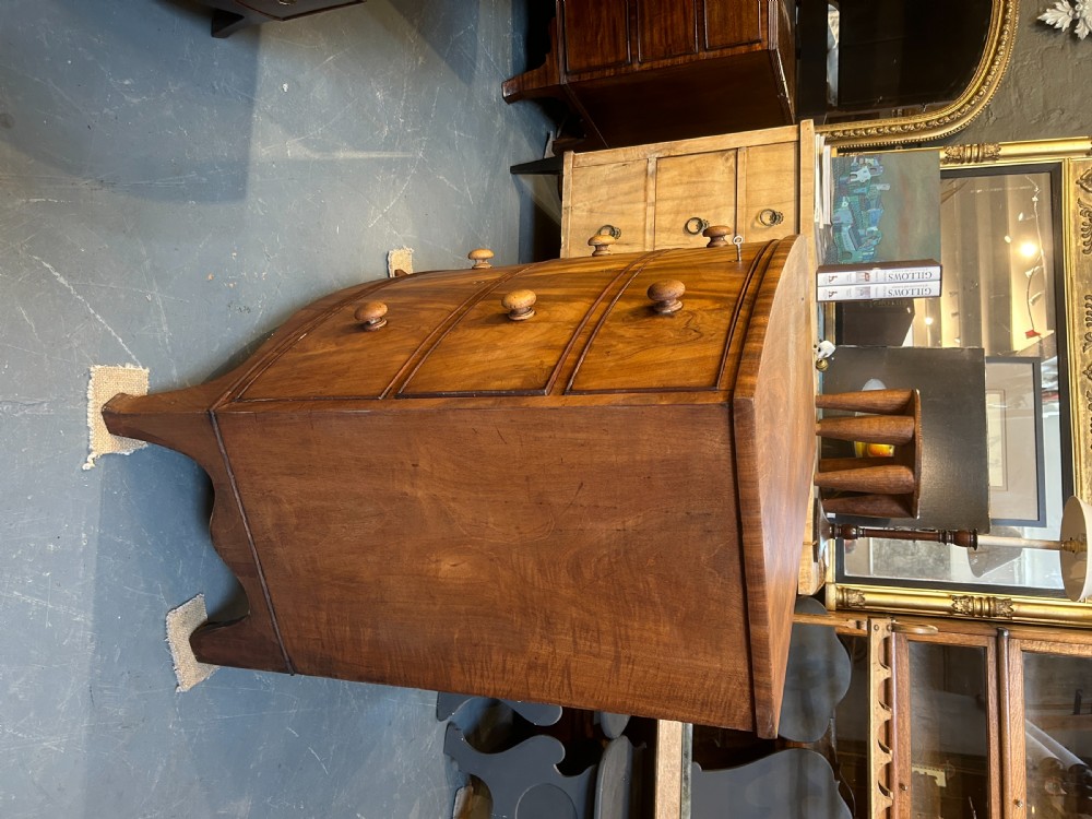 A George III bow front chest of drawers in warm brown timber, featuring three graduated drawers with turned wooden handles and splayed feet. View IX