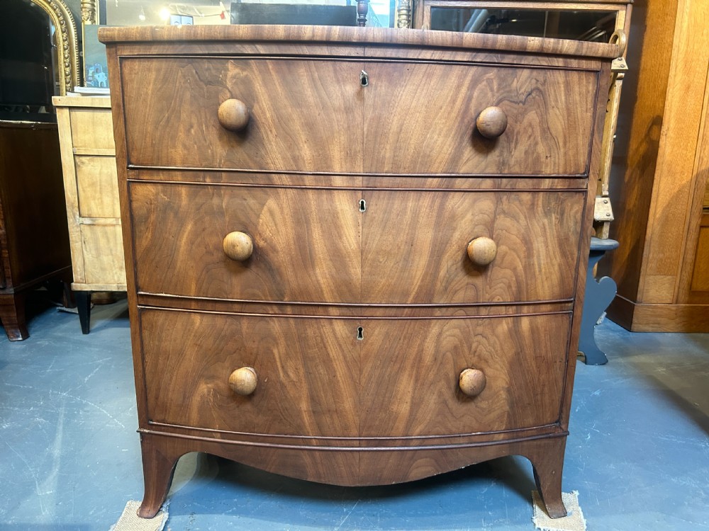 A George III bow front chest of drawers in warm brown timber, featuring three graduated drawers with turned wooden handles and splayed feet. View XII