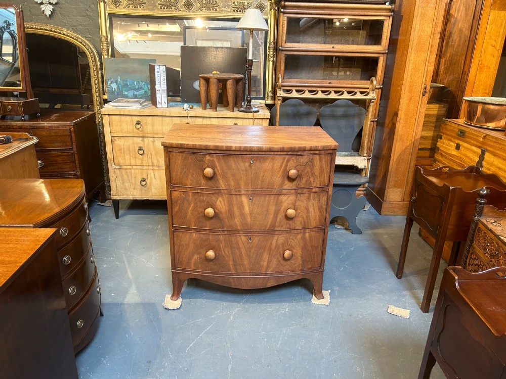 A George III bow front chest of drawers in warm brown timber, featuring three graduated drawers with turned wooden handles and splayed feet. View XIII