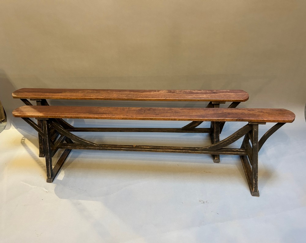A pair of long wooden benches featuring natural polished brown wooden seats supported by dark ebonised trestle bases.