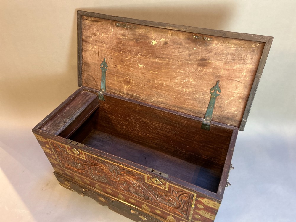 A 19th-century dark hardwood Zanzibar chest featuring relief floral carving, pierced brass plates, brass corner mounts, and three small lower drawers. View II