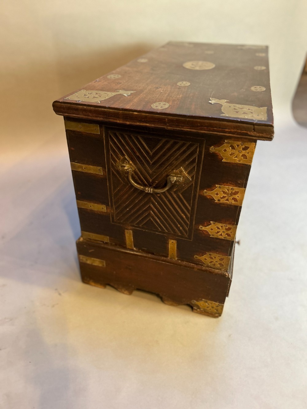 A 19th-century dark hardwood Zanzibar chest featuring relief floral carving, pierced brass plates, brass corner mounts, and three small lower drawers. View V