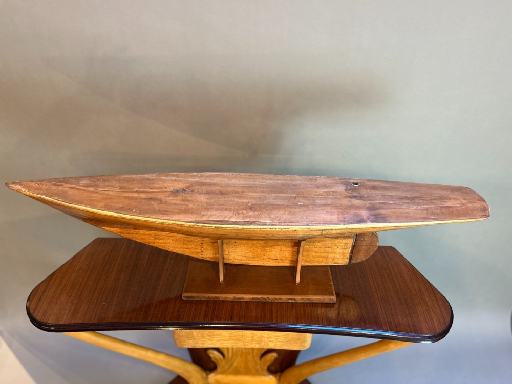 A varnished wooden pond yacht hull supported upright on a custom wooden display stand. View III