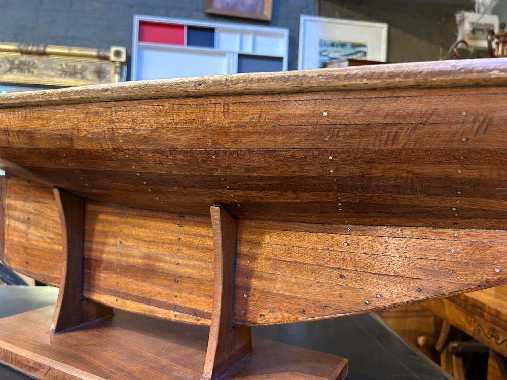 A varnished wooden pond yacht hull supported upright on a custom wooden display stand. View VIII