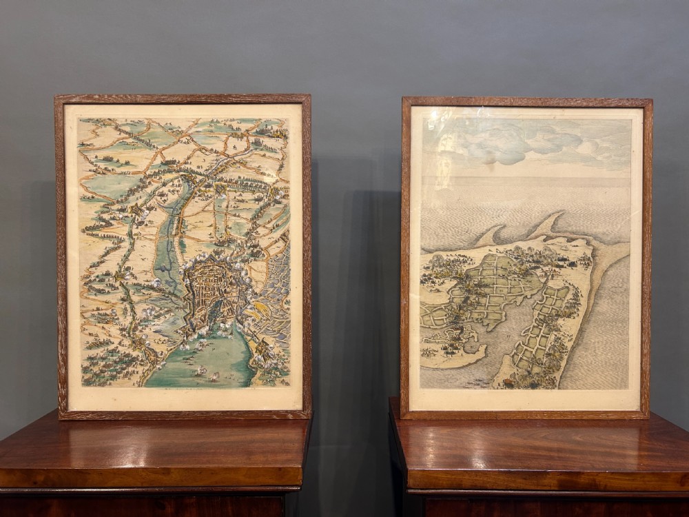A pair of framed 19th-century prints displaying detailed topographical military formations and coastal maps in matching wooden frames.