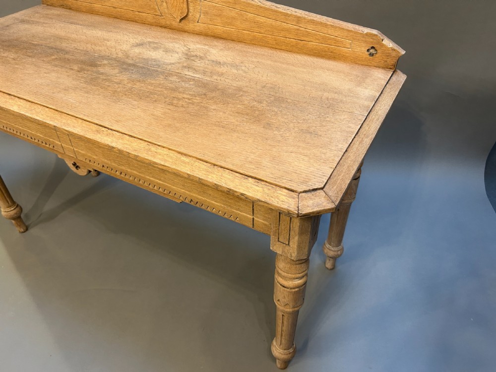 A Victorian light oak hall table featuring a carved upstand with a central shield motif, decorative frieze, and turned legs. View II