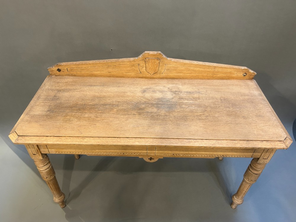 A Victorian light oak hall table featuring a carved upstand with a central shield motif, decorative frieze, and turned legs. View V