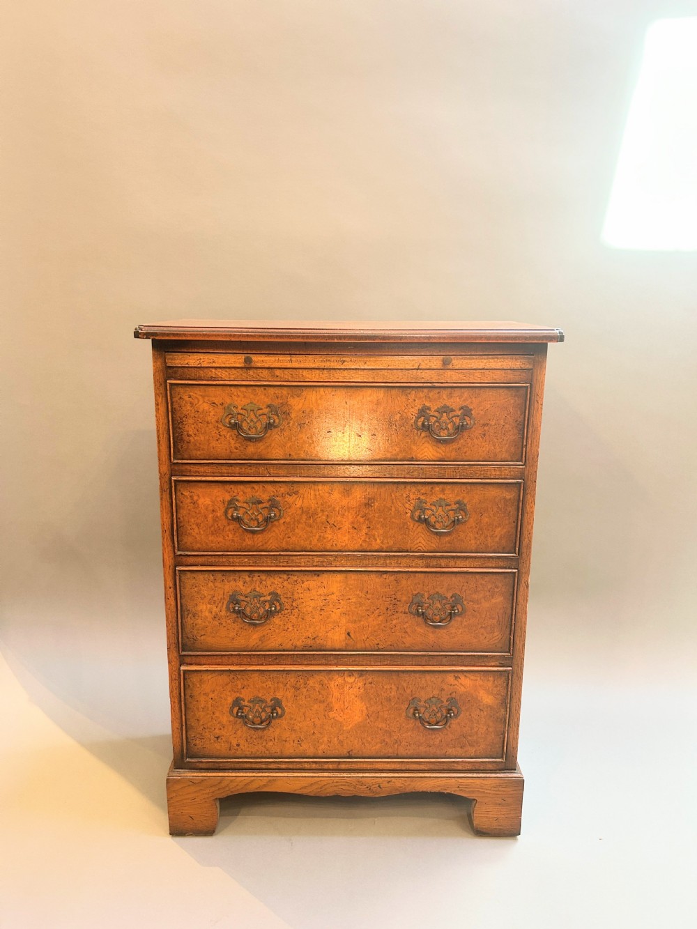 A small Georgian Revival burr walnut chest of drawers featuring four graduated drawers with brass drop handles and bracket feet. View II