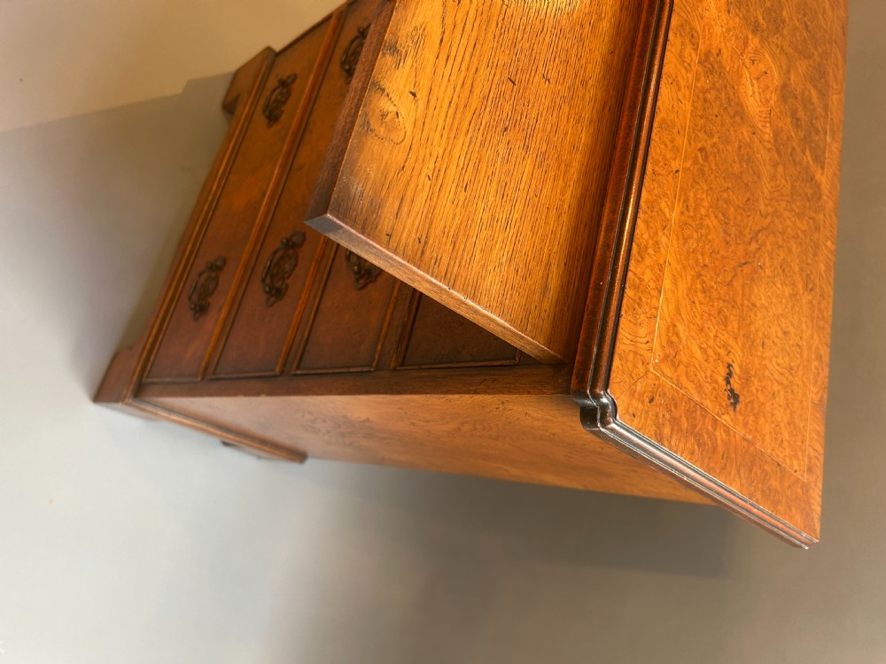 A small Georgian Revival burr walnut chest of drawers featuring four graduated drawers with brass drop handles and bracket feet. View III