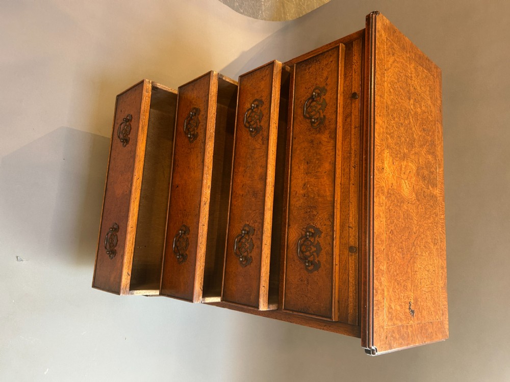 A small Georgian Revival burr walnut chest of drawers featuring four graduated drawers with brass drop handles and bracket feet. View IV