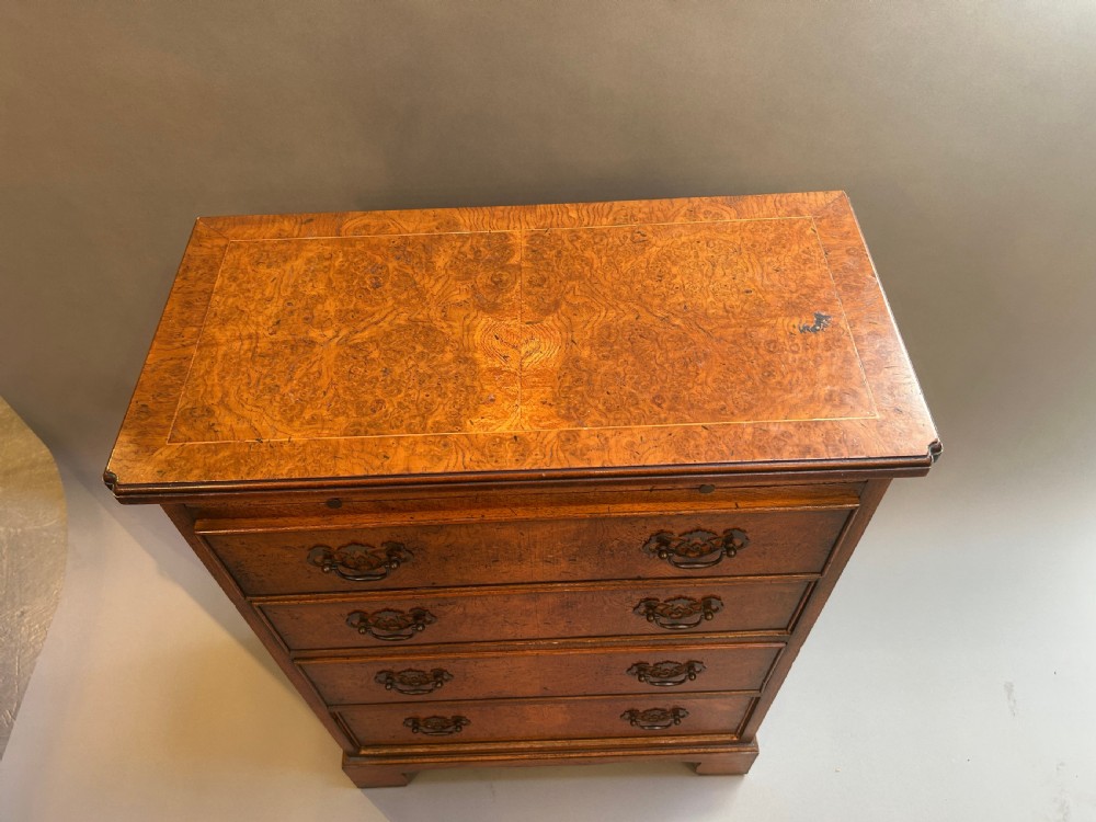A small Georgian Revival burr walnut chest of drawers featuring four graduated drawers with brass drop handles and bracket feet. View V