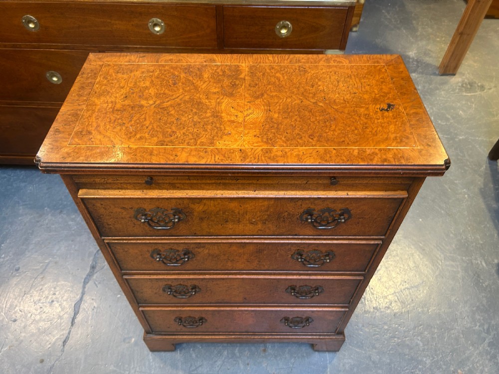 A small Georgian Revival burr walnut chest of drawers featuring four graduated drawers with brass drop handles and bracket feet. View VIII