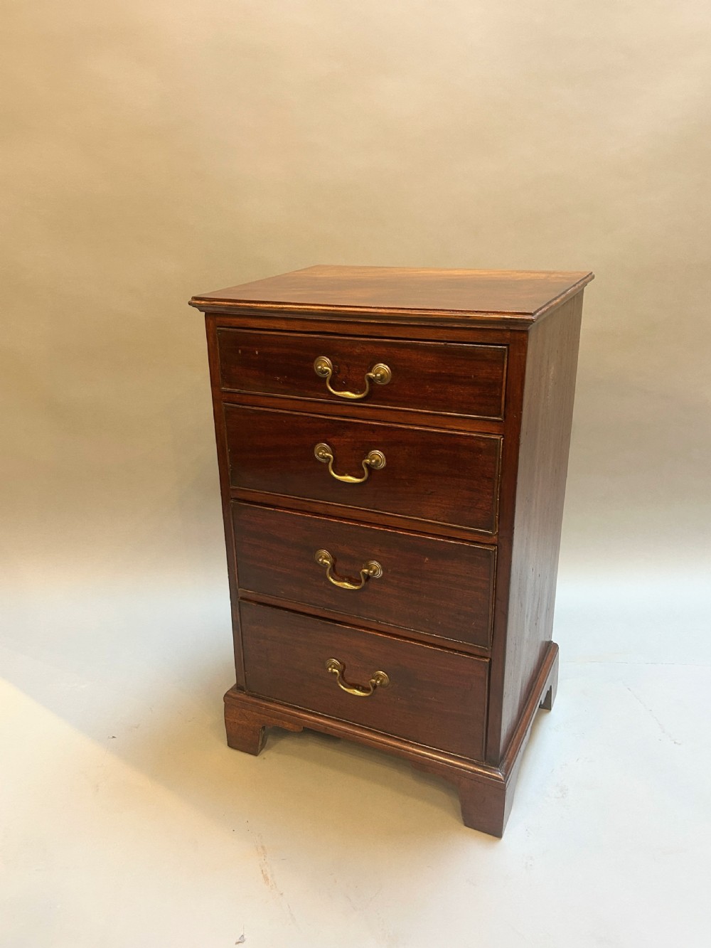 A compact antique mahogany pedestal chest featuring four drawers with brass swan-neck handles and bracket feet.