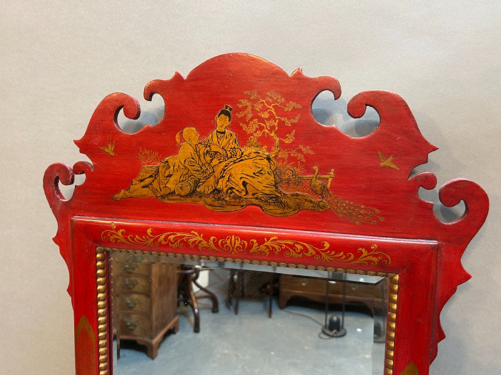 A tall rectangular red lacquered wall mirror featuring intricate gilt Chinoiserie motifs and a scrolled carved pediment. View II