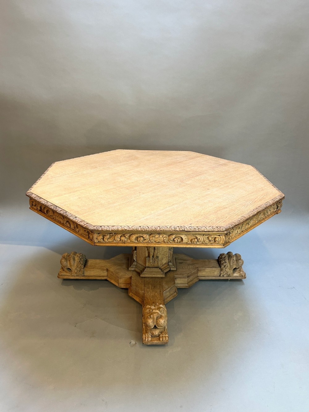 An octagonal Victorian carved oak breakfast table featuring a carved frieze and a central pedestal base supported by four carved lion feet.