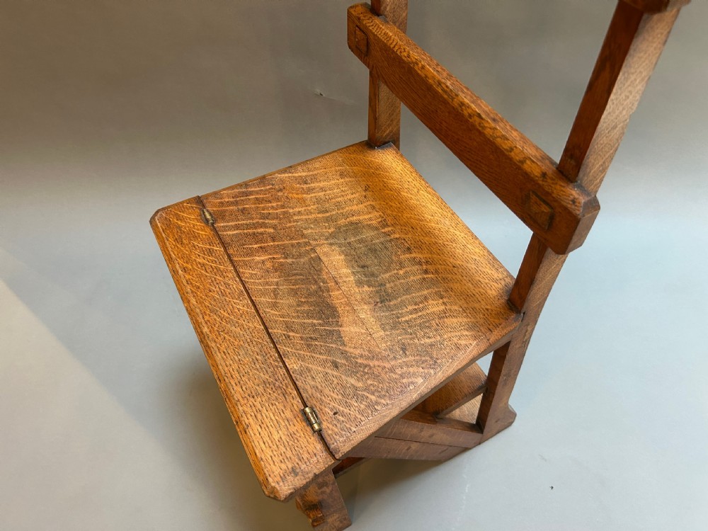An antique solid oak metamorphic chair that folds into library steps, featuring a pierced trefoil motif backrest and square legs. View II