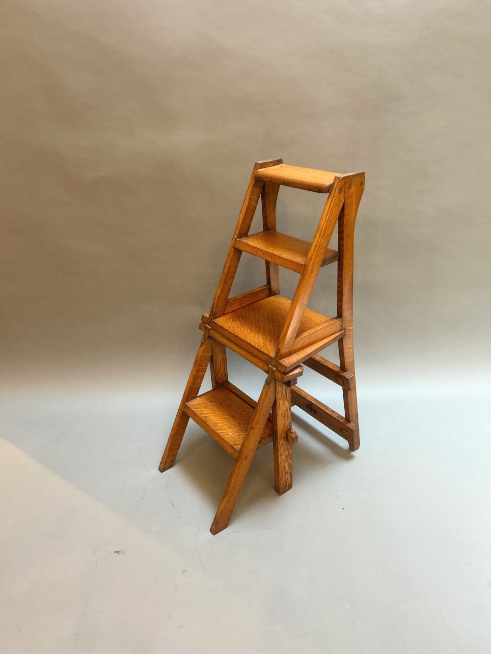 An antique solid oak metamorphic chair that folds into library steps, featuring a pierced trefoil motif backrest and square legs. View VII