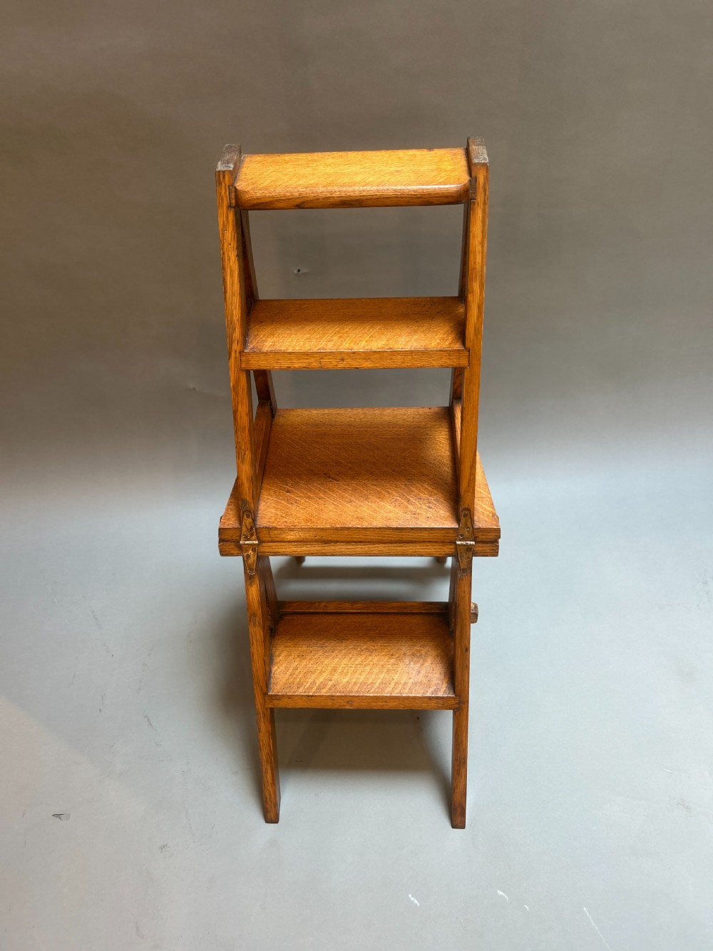 An antique solid oak metamorphic chair that folds into library steps, featuring a pierced trefoil motif backrest and square legs. View X