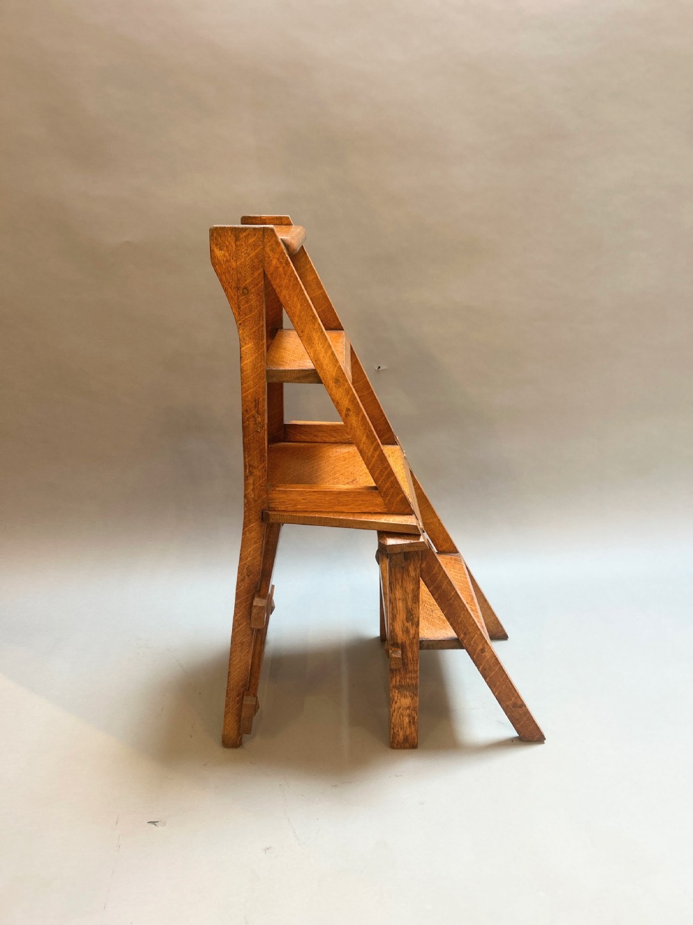 An antique solid oak metamorphic chair that folds into library steps, featuring a pierced trefoil motif backrest and square legs. View XI