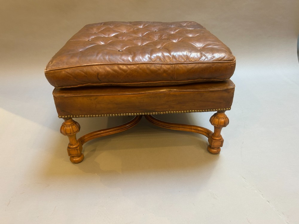 A square chestnut brown leather footstool featuring deep button tufting, brass stud trimming, and carved wooden legs with curved stretchers. View IV