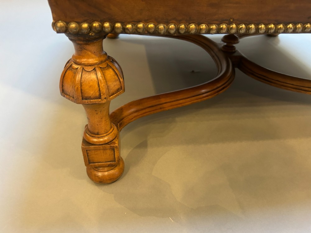 A square chestnut brown leather footstool featuring deep button tufting, brass stud trimming, and carved wooden legs with curved stretchers. View V