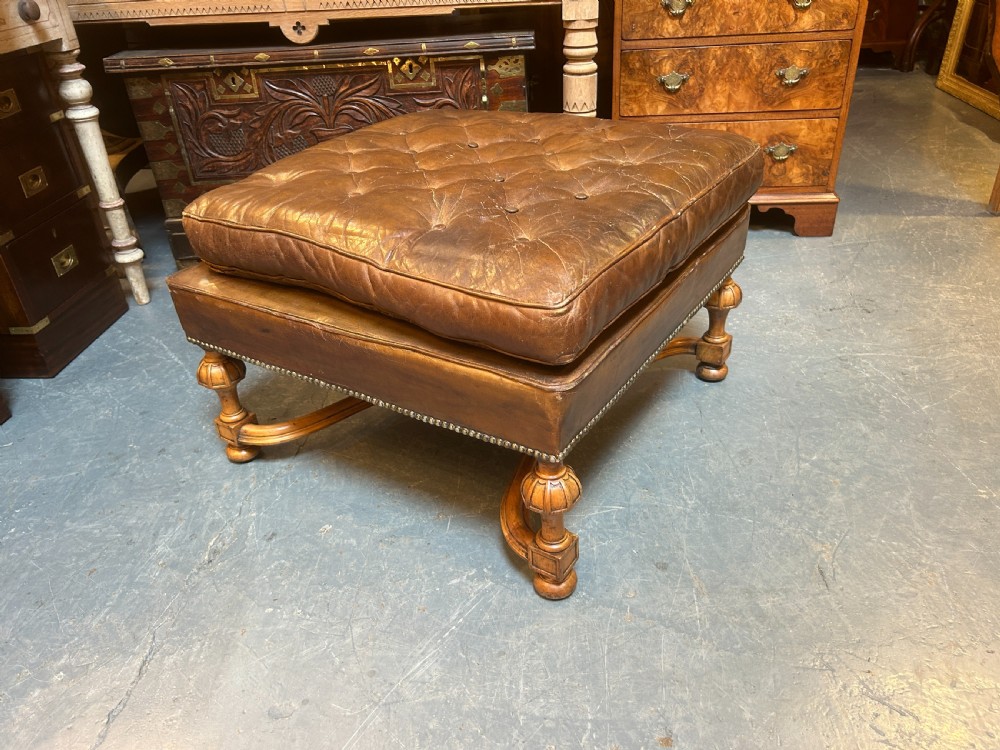 A square chestnut brown leather footstool featuring deep button tufting, brass stud trimming, and carved wooden legs with curved stretchers. View VIII