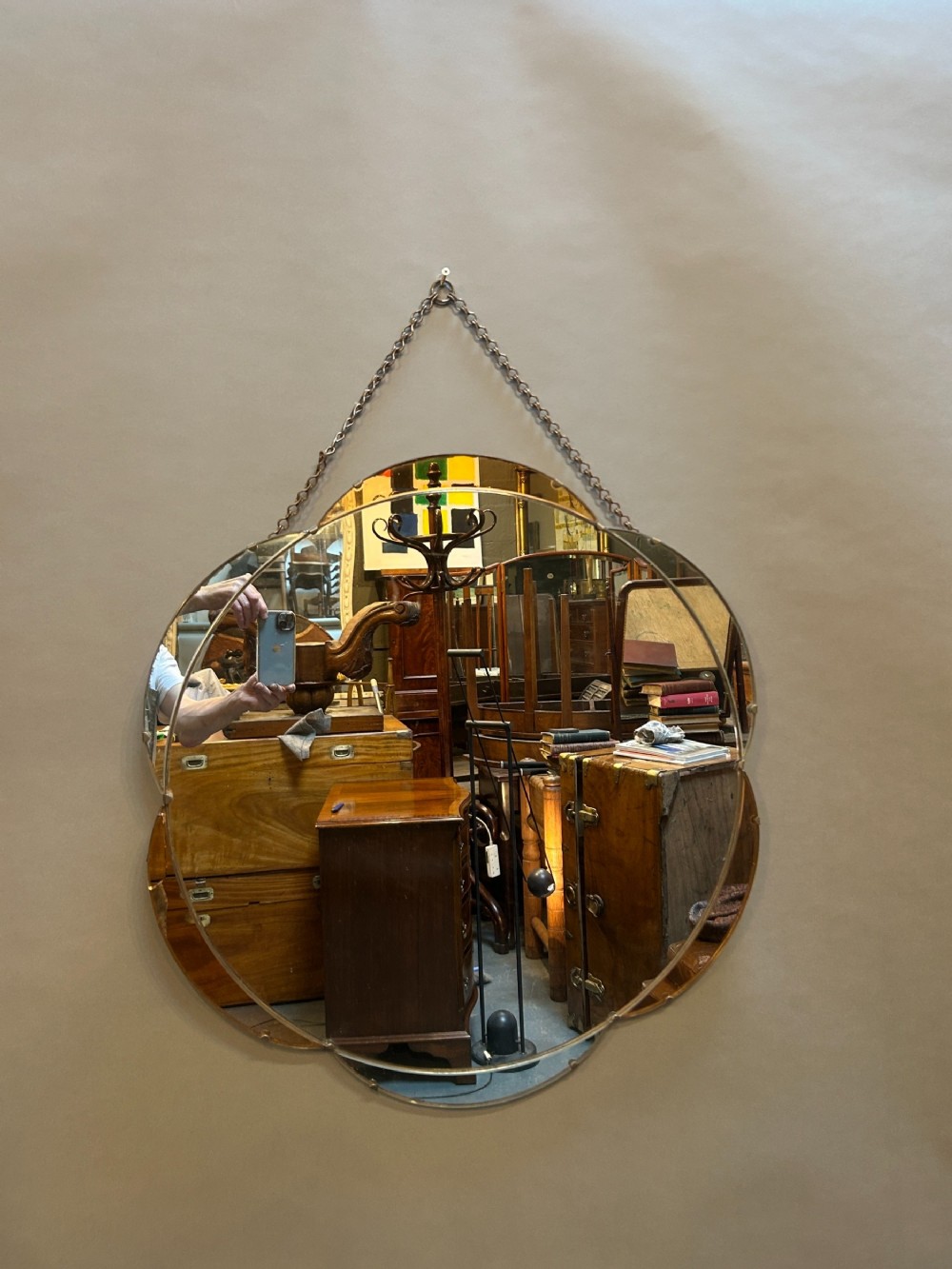 A circular Art Deco wall mirror featuring scalloped outer sectional mirror panels and suspended by a metal hanging chain.
